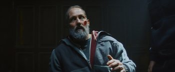 Movie still from “Lost Bullet 2: Back for More” (2022), directed by Guillaume Pierret – A man with a gray beard and a red bandage on his face; Close Up shot, Low angle
