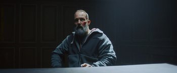 Movie still from “Lost Bullet 2: Back for More” (2022), directed by Guillaume Pierret – A man with a gray beard and a red bandage on his face; Medium shot, Over the shoulder angle