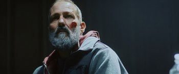 Movie still from “Lost Bullet 2: Back for More” (2022), directed by Guillaume Pierret – An older man with a beard and a red nose; Close Up shot, Low angle