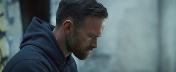 Movie still from “Lost Bullet 2: Back for More” (2022), directed by Guillaume Pierret – A person with a beard looking down; Close Up shot, Over the shoulder angle