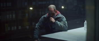 Movie still from “Lost Bullet 2: Back for More” (2022), directed by Guillaume Pierret – A man sitting at a table with his hand on his face; Medium shot, Low angle