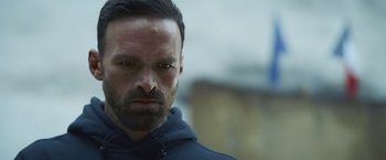 Movie still from “Lost Bullet 2: Back for More” (2022), directed by Guillaume Pierret – A person wearing a hoodie; Close Up shot, Low angle