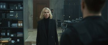 Movie still from “Lost Bullet 2: Back for More” (2022), directed by Guillaume Pierret – A woman in a black suit standing in a room; Medium shot, Over the shoulder angle
