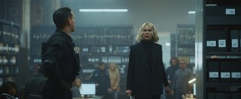 Movie still from “Lost Bullet 2: Back for More” (2022), directed by Guillaume Pierret – A woman in a black jacket and a man in a black suit stand next to each other in a room; Medium shot, Over the shoulder angle