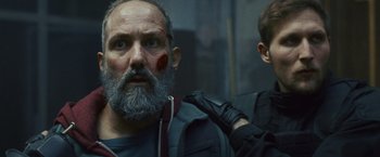 Movie still from “Lost Bullet 2: Back for More” (2022), directed by Guillaume Pierret – A person with a beard and face paint; Close Up shot, Over the shoulder angle