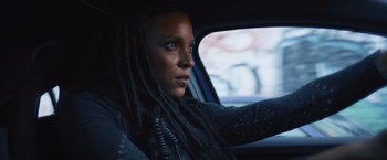 Movie still from “Lost Bullet 2: Back for More” (2022), directed by Guillaume Pierret – A woman with dreads sitting in the driver's seat of a car; Close Up shot, Over the shoulder angle