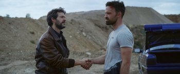 Movie still from “Lost Bullet 2: Back for More” (2022), directed by Guillaume Pierret – Two men shaking hands on a dirt field; Medium shot, Over the shoulder angle