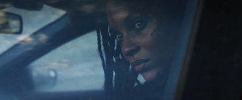 Movie still from “Lost Bullet 2: Back for More” (2022), directed by Guillaume Pierret – A person with dreadlocks in a car; Close Up shot, Over the shoulder angle