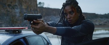 A woman with dreadlocks is holding a gun in her hand