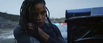 Movie still from “Lost Bullet 2: Back for More” (2022), directed by Guillaume Pierret – A woman with dreadlocks is looking at the camera; Close Up shot, Over the shoulder angle