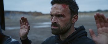 Movie still from “Lost Bullet 2: Back for More” (2022), directed by Guillaume Pierret – A person with blood on his face; Close Up shot, Over the shoulder angle