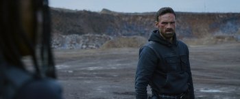 Movie still from “Lost Bullet 2: Back for More” (2022), directed by Guillaume Pierret – A man in a black jacket standing in a field; Medium shot, Over the shoulder angle