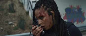 Movie still from “Lost Bullet 2: Back for More” (2022), directed by Guillaume Pierret – A woman with dreadlocks is talking on a walkie talkie; Close Up shot, Over the shoulder angle