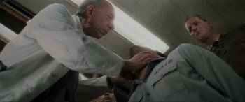 Movie still from “Lost Highway” (1997), directed by David Lynch – An older man is helping a younger man put on a uniform; Close Up shot, Low angle