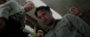 Movie still from “Lost Highway” (1997), directed by David Lynch – A person in a room with other people; Close Up shot, Low angle