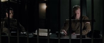 Movie still from “Lost Highway” (1997), directed by David Lynch – A man sitting at a table in front of a jail cell; Medium shot, High angle