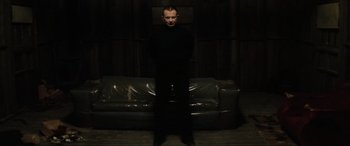 Movie still from “Lost Highway” (1997), directed by David Lynch – A man standing in front of a couch in a dark room; Wide shot, Low angle