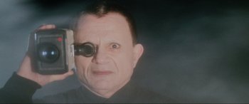 Movie still from “Lost Highway” (1997), directed by David Lynch – A man looking through a magnifying glass at something; Close Up shot, Low angle