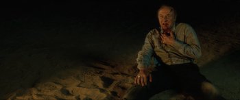 Movie still from “Lost Highway” (1997), directed by David Lynch – A man sitting on the ground in the dark; Medium shot, High angle