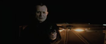 Movie still from “Lost Highway” (1997), directed by David Lynch – A man holding a gun while standing in a dark room; Close Up shot, Over the shoulder angle