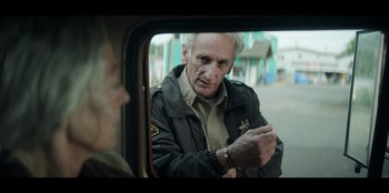 Movie still from “Lou” (2022), directed by Anna Foerster – An older man looking at his cell phone in the mirror of a car; Close Up shot, Over the shoulder angle