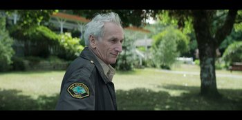 Movie still from “Lou” (2022), directed by Anna Foerster – An older man in a jacket is standing in a park; Close Up shot, Over the shoulder angle