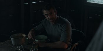 Movie still from “Lou” (2022), directed by Anna Foerster – A man sitting at a table with a bowl of food; Medium shot, Over the shoulder angle