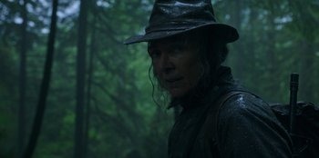 Movie still from “Lou” (2022), directed by Anna Foerster – A person wearing a hat in the rain with trees in the background; Close Up shot, Low angle