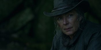 Movie still from “Lou” (2022), directed by Anna Foerster – An older woman wearing a hat in the woods; Close Up shot, Over the shoulder angle