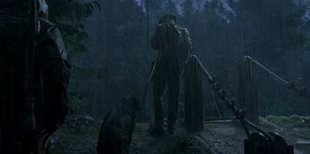 Movie still from “Lou” (2022), directed by Anna Foerster – A man standing in the rain next to a bear; Wide shot, Low angle