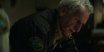 Movie still from “Lou” (2022), directed by Anna Foerster – An older man wearing a uniform looking down; Close Up shot, Over the shoulder angle