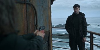 Movie still from “Lou” (2022), directed by Anna Foerster – A man standing next to the ocean while holding a cell phone; Medium shot, Over the shoulder angle