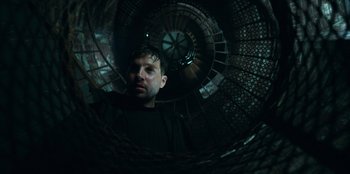 Movie still from “Lou” (2022), directed by Anna Foerster – A man standing inside of a spiral staircase; Close Up shot, Low angle