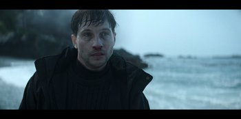 Movie still from “Lou” (2022), directed by Anna Foerster – A person wearing a jacket near a body of water; Close Up shot, Low angle