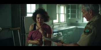 Movie still from “Lou” (2022), directed by Anna Foerster – A woman in a pink shirt is holding a book; Medium shot, Over the shoulder angle