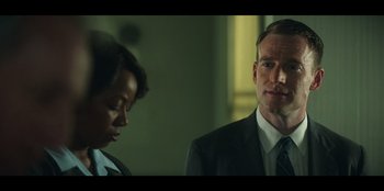 Movie still from “Lou” (2022), directed by Anna Foerster – A man in a suit standing next to a woman in a suit; Close Up shot, Over the shoulder angle