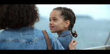 Movie still from “Lou” (2022), directed by Anna Foerster – A young girl is smiling while holding her mother's shoulder; Close Up shot, Over the shoulder angle