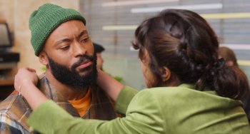Movie still from “Love Again” (2023), directed by Jim Strouse – A man with a beard and a green hat is getting his face painted by a woman; Close Up shot, Over the shoulder angle