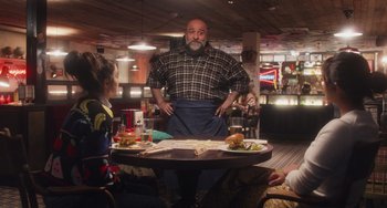 Movie still from “Love Again” (2023), directed by Jim Strouse – A man standing at a table in front of a group of diners; Medium shot, Over the shoulder angle