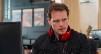 Movie still from “Love Again” (2023), directed by Jim Strouse – A man with red headphones sitting in front of a tv; Close Up shot, Over the shoulder angle