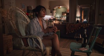 Movie still from “Love Again” (2023), directed by Jim Strouse – A woman sitting in a chair holding a glass of wine; Wide shot, High angle