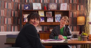 Movie still from “Love Again” (2023), directed by Jim Strouse – Two women sitting at a table in front of a book shelf; Medium shot, Over the shoulder angle