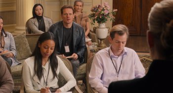 Movie still from “Love Again” (2023), directed by Jim Strouse – A group of people sitting in a living room; Medium shot, Over the shoulder angle