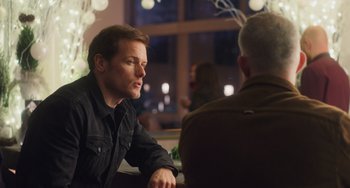 Movie still from “Love Again” (2023), directed by Jim Strouse – A man sitting in front of another man at a table; Medium shot, Over the shoulder angle