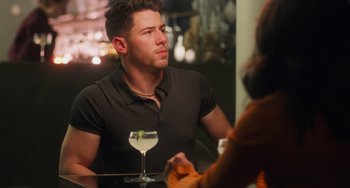 Movie still from “Love Again” (2023), directed by Jim Strouse – A man sitting at a table in front of a glass of wine; Medium shot, Over the shoulder angle