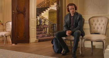 Movie still from “Love Again” (2023), directed by Jim Strouse – A man sitting on top of a chair wearing headphones; Medium shot, Low angle