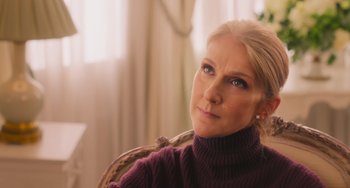 Movie still from “Love Again” (2023), directed by Jim Strouse – A woman sitting in a chair looking at the camera; Close Up shot, Over the shoulder angle