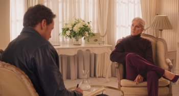 Movie still from “Love Again” (2023), directed by Jim Strouse – A man and a woman sitting in a living room; Medium shot, Over the shoulder angle