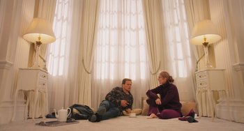 Movie still from “Love Again” (2023), directed by Jim Strouse – A man and a woman sitting on the floor in front of a window; Wide shot, High angle