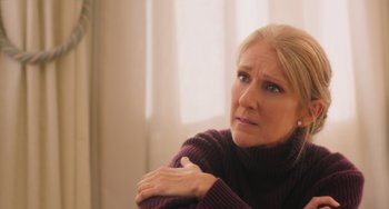 Movie still from “Love Again” (2023), directed by Jim Strouse – A blonde woman in a purple sweater looking at the camera; Close Up shot, Over the shoulder angle